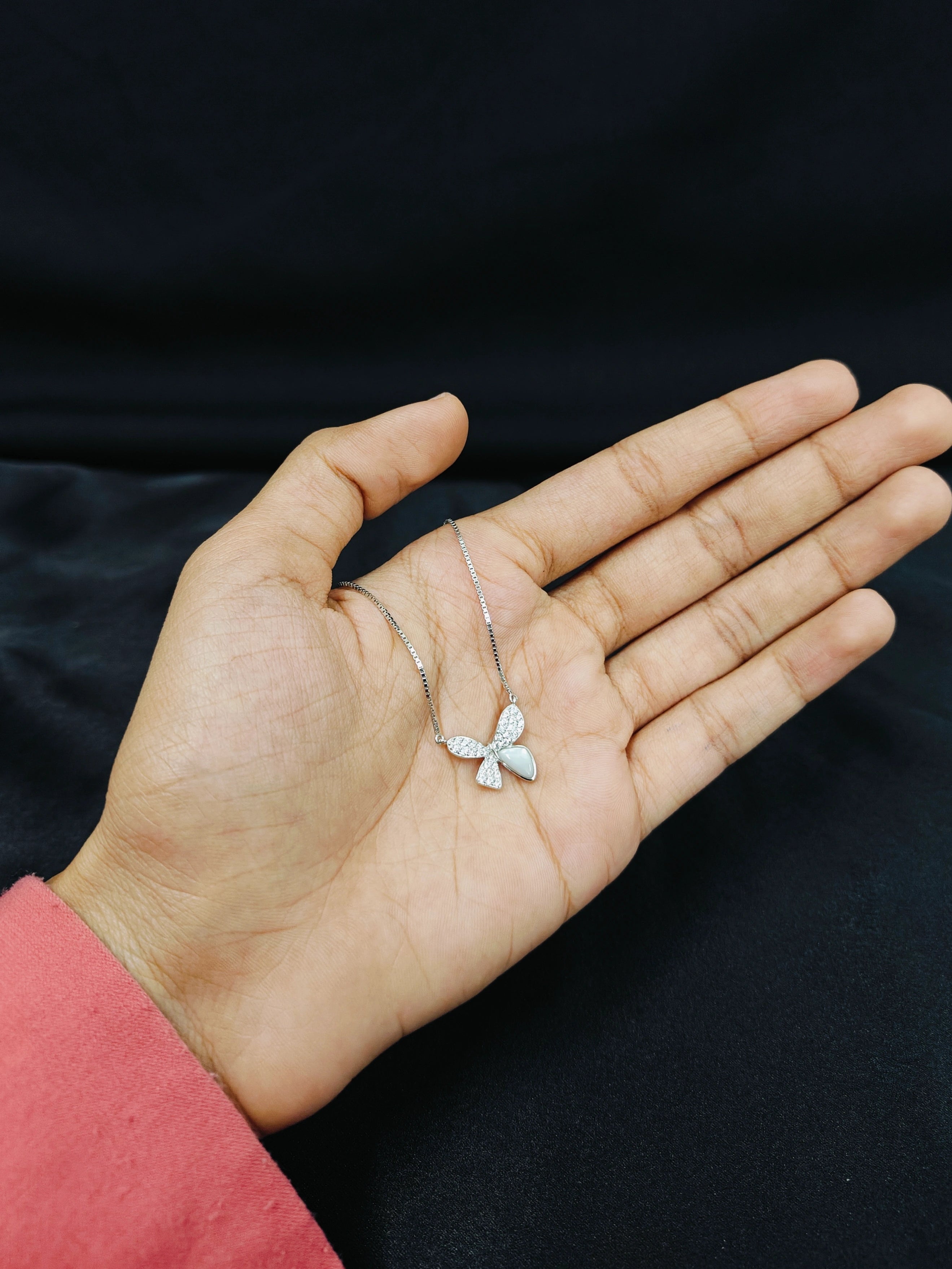 Hand holding a delicate silver necklace against a black background